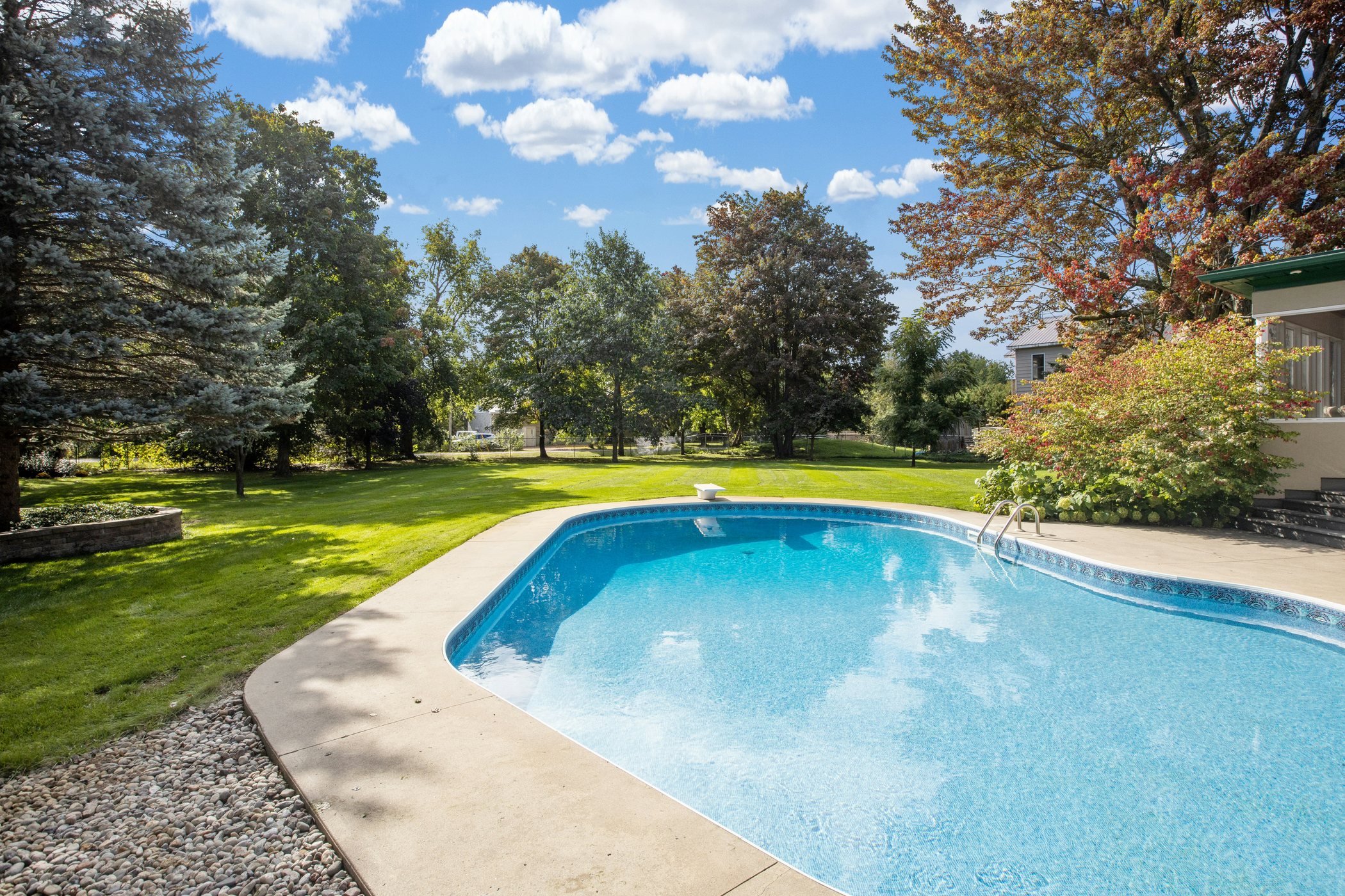 Residential backyard swimming pool with lawn, trees, and deck